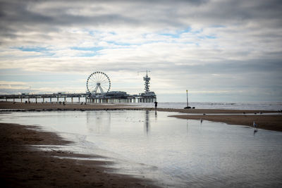 Ferris wheel at beach against cloudy sky