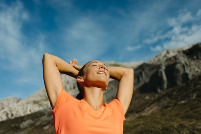 Midsection of young woman with arms raised against sky