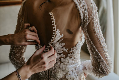 Cropped hands of woman assisting bride while getting dressed