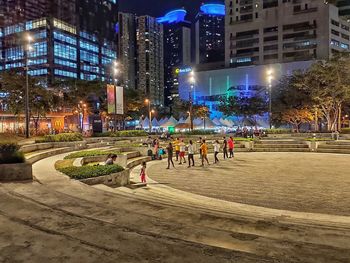 People on street against illuminated buildings at night