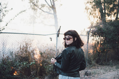 Portrait of young woman standing against fence