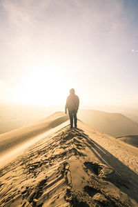 Rear view of man standing on sand dune against sky during sunset