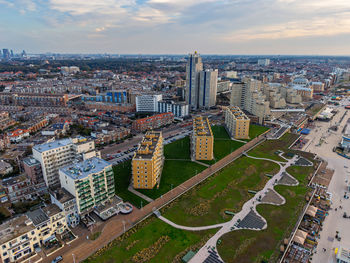 Aerial view of coastal city with angular golden brown buildings on green lawn, beach promenade