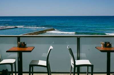 Empty chairs and table by sea against clear sky