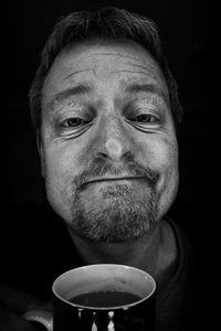 Close-up portrait of man holding coffee cup against black background