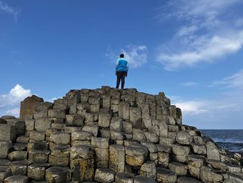 Rear view of man standing on rock by sea against sky