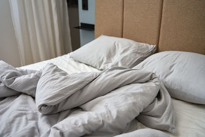 Crumpled bed with pillows, blanket and crumpled sheets in bedroom