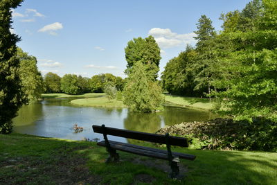 Bench by lake against sky