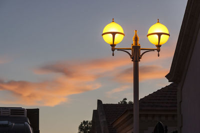 Low angle view of illuminated street light by building against sky