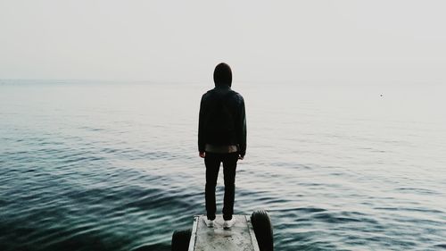 Rear view of person standing on pier at sea