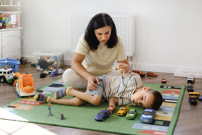 Disabled boy playing toy cars with mother at home. cerebral palsy child entertaining on the mat