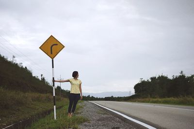 Woman standing by road sign against sky