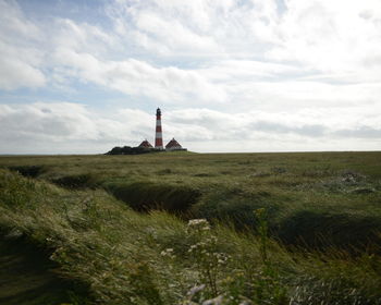 Lighthouse on field against cloudy sky