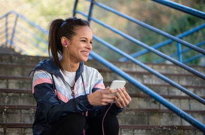 Young woman looking away while listening music through mobile phone