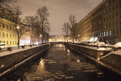 Illuminated street amidst buildings in city during winter