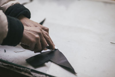 Cropped hands of tailor cutting fabric with cutter on table