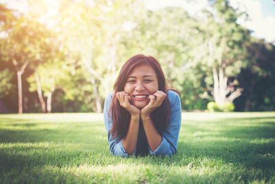 Portrait of happy young woman lying on grass at park