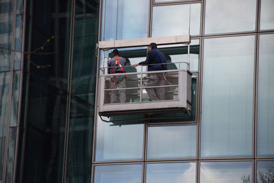 Low angle view of window washers cleaning glass building