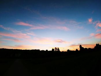 Silhouette trees on field against sky during sunset