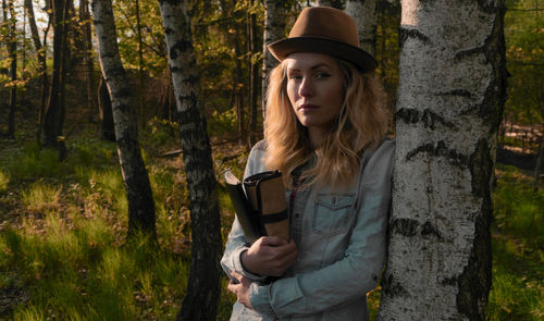 Portrait of woman standing by tree trunk in forest