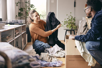 Happy woman showing shirt to man while sorting clothes at home