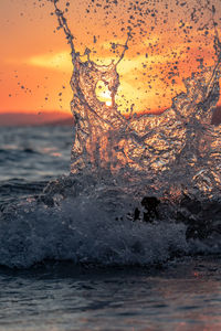 Water splashing in sea against sky during sunset