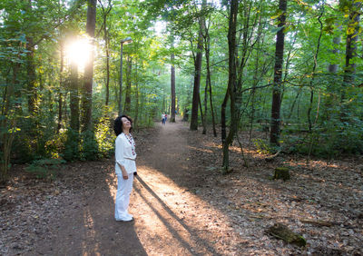 Happy woman standing on dirt road against trees in forest