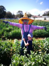 Girl holding scarecrow while standing amidst plants on field