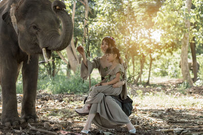 Woman with daughter touching elephant in forest