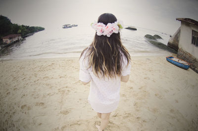 Rear view of woman with flowers on hair standing at sandy beach