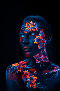 Close-up of woman with illuminated body paint against black background