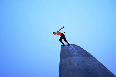 Low angle view of man jumping against clear blue sky