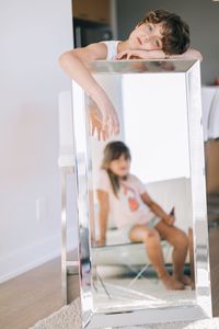 Portrait of girl holding mirror with reflection of sister at home