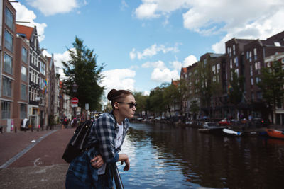 Man standing by canal in city against sky