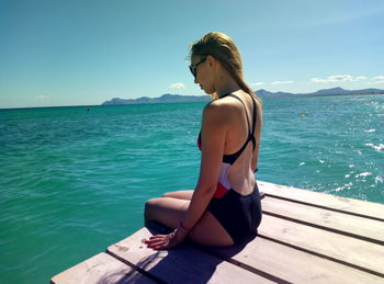 Young woman sitting on pier over sea against sky