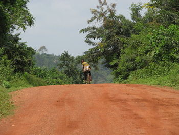 Rear view of man looking over shoulder while riding bicycle on dirt road at field