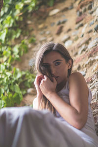 Portrait of young woman sitting against brick wall