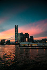 Scenic view of river by buildings against sky at sunset