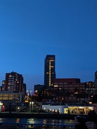 Illuminated buildings by river against blue sky