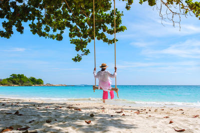Rear view of woman swinging at beach against sky