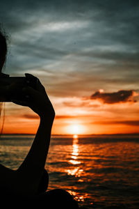 Silhouette man in sea against sky during sunset