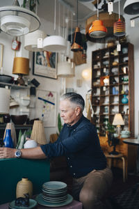 Senior male owner arranging merchandise while sitting at antique store