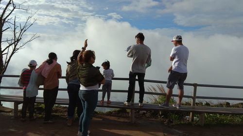 Rear view of people standing by railing against sky