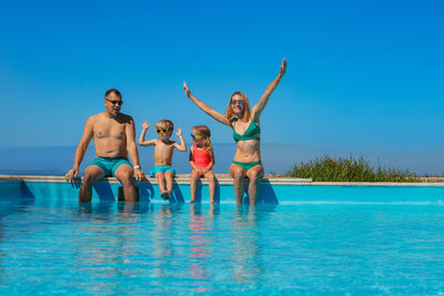 Young woman with arms raised jumping in swimming pool