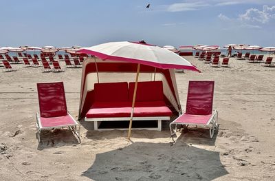 Empty chairs on beach against sky