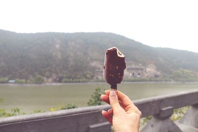 Cropped hand of woman holding chocolate ice cream against sky