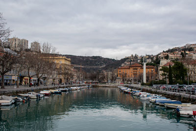 Boats moored in river by buildings in city against sky