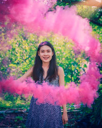 Portrait of a smiling young woman standing against pink plants