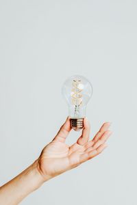 Close-up of hand holding light bulb against white background