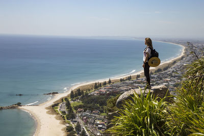 Female backpacker, standing on top of mount maunganui, looking at view